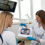 The dentist shows the x-ray image to the patient. People, medicine, dentistry, technology and healthcare concept. Woman dentist with x-ray image of teeth and female patient in dental clinic office.