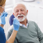 Doctor checking up patient's teeth at dentist office; senior man at dental checkup